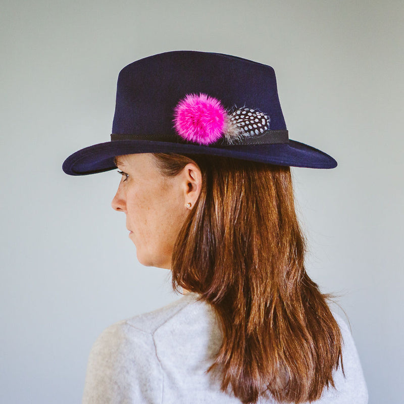 navy blue wool felt fedora with black leather band fuchsia pink fur pom pom and black and white guinea fowl feather
